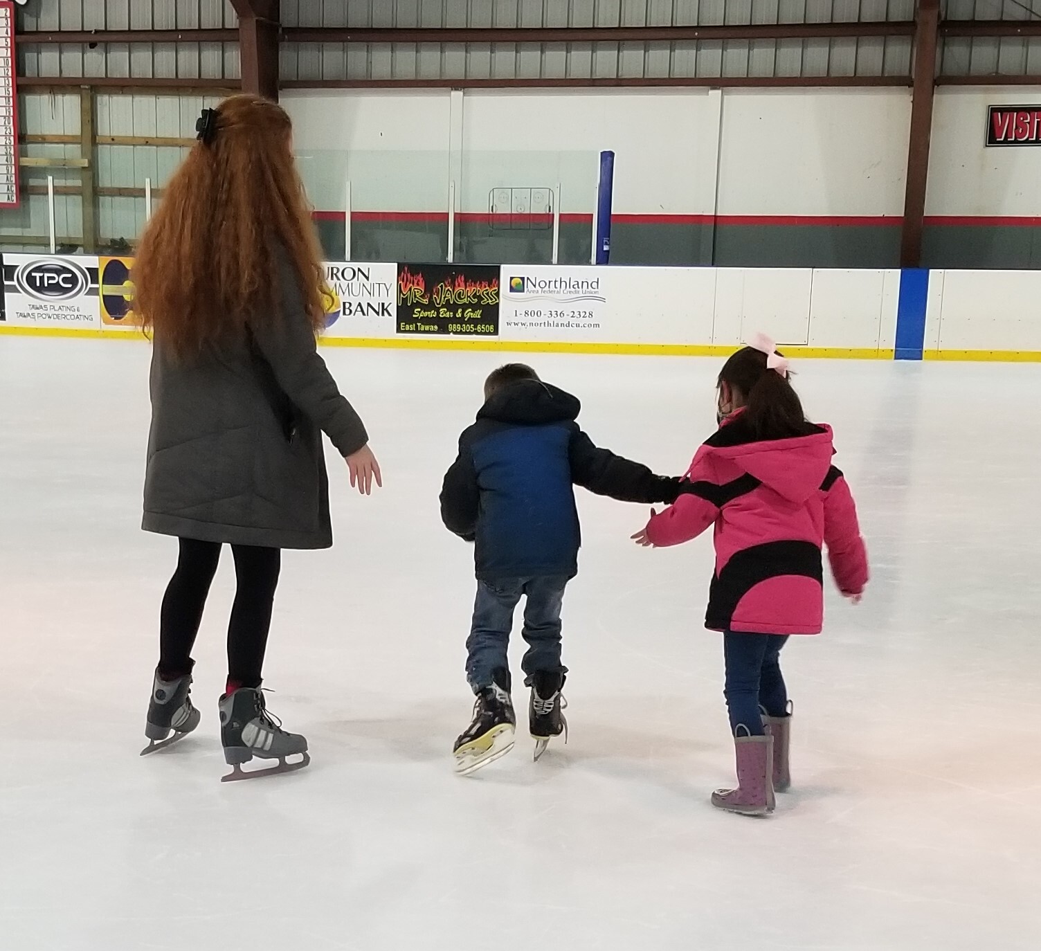 HS student teaching children to ice skate.