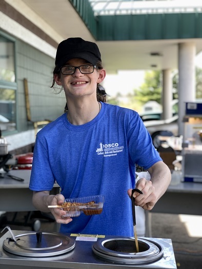 Culinary student who was working the concession area at the recent Mudslinger event is dipping chocolate to put on waffle stick.