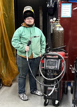 Student standing with his welder by the welding booth.