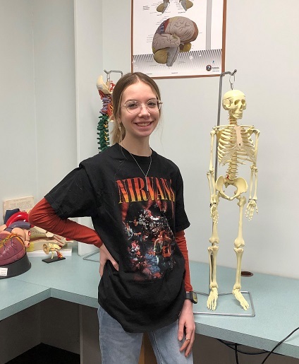 Picture of health science student, Addison Ludwig, standing next to a skeleton.