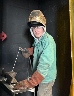 Student in a welding booth posing as if welding.