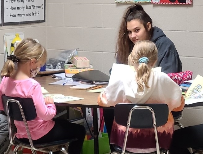 Student of the Month, Kylie Sizemore, is sitting at a table working with elementary students.