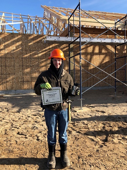 Building Trades student standing in front of the house they are building. Holding his award and coffee mug.
