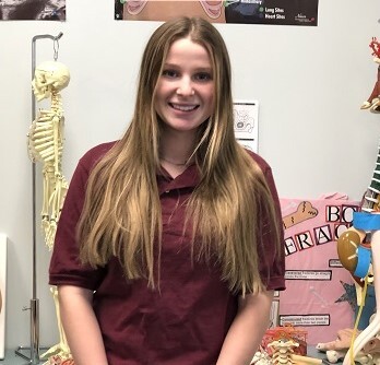 Health Science student standing in front of skeleton and posters.